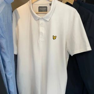Vit piké t-shirt från Lyle & Scott - Vit piké t-shirt från Lyle & Scott med klassisk krage och tre knappar framtill. Perfekt för en clean och stilren look.