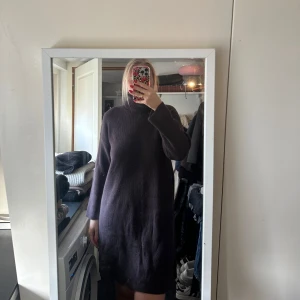 Mörk stickad långärmad klänning - Mysig mörk stickad klänning med lång ärm och hög hals. Klänningen har en rak passform och slutar ovanför knäna. Perfekt för kyligare dagar och enkel att styla med boots eller sneakers.