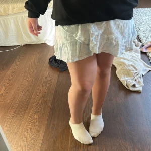  baby ljus blå volangkjol - Säljer en ljusblå kortkjol med volangdetaljer. Kjolen har en luftig och lätt struktur, perfekt för varmare dagar. Den har en omlottliknande volang framtill som ger en söt och trendig look.