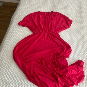 Cerise långklänning från MNG - Säljer en cerise långklänning från MNG med korta ärmar och markerad midja. Klänningen har en enkel och elegant design, perfekt för sommarens tillfällen. Materialet känns mjukt och följsamt mot huden.