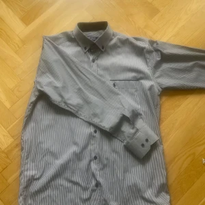 Randig skjorta från Polo Ralph Lauren - Klassisk skjorta från Polo Ralph Lauren i vitt och grått med tunna ränder. Skjortan har lång ärm, knappar framtill och en bröstficka med broderad logga. Perfekt till dig som gillar stilrena plagg med snygga detaljer. Hör gärna av er vid frågor och funderingar! 