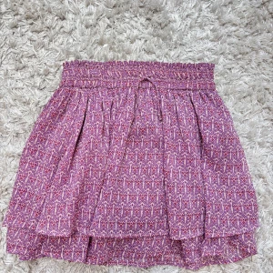 Rosa mönstrad kortkjol från Zara - Supersöt rosa kortkjol från Zara med småmönstrat tryck och smock i midjan. Kjolen har volangdetaljer och är perfekt för dig som gillar färg och mönster. Lätt och luftig modell som passar till många olika stilar.