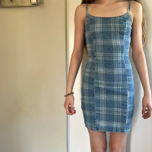 Blå rutig klänning från H&M Divided - Supersöt blå rutig klänning från H&M Divided med smala axelband och tight passform. Klänningen har dragkedja på sidan och är i ett mjukt jeanstyg. Perfekt för dig som gillar en enkel men trendig stil.