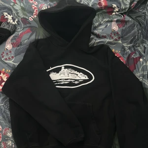 Svart hoodie med tryck - Säljer en svart hoodie i storlek XS med vit tryckt grafik på bröstet. Tröjan har huva och magficka, perfekt för en avslappnad stil. Materialet känns mjukt och bekvämt.