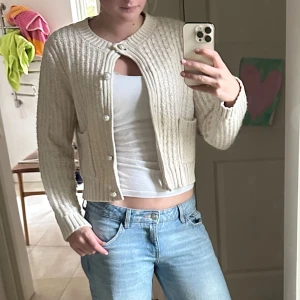 Beige stickad kofta från Kappahl - Säljer en beige stickad kofta från Kappahl med pärlknappar och två fickor framtill. Säljer då den inte kommer till användning 