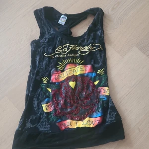 Svart linnetopp med Ed Hardy-tryck - Skitasnyggt ed hardy linne! Tröjan saknar pärlor och de trillar av om du rör dem! Ek slags knytning där bak på ryggen också. 