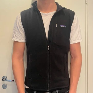 Patagonia väst  - Säljer en svart fleeceväst från Patagonia med dragkedja framtill och bröstficka med logga. Västen är i mjuk polyester och har en klassisk passform. Perfekt till sommar och vår.