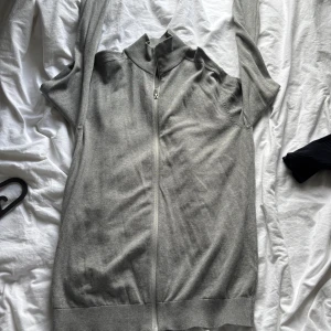 Grå ziptröja från Selected Homme - Säljer en stilren grå ziptröja från Selected Homme. Tröjan har hög krage, hel dragkedja framtill och ribbade muddar. Perfekt för lager-på-lager och enkel att matcha med andra plagg.