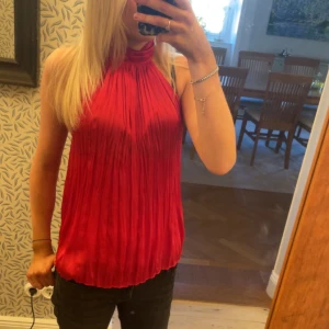 Röd halterneck-top -  Jag säljer en röd halterneck-top med hög krage som knäpps med knappar i nacken. Toppen är ärmlös och har en elegant, lös passform. Köpt i Italien förra våren. Passar till våren och sommar jätte bra.