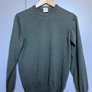 Mörkgrå stickad tröja från Adverb - En enkel och stilren mörkgrå stickad tröja från Adverb. Tröjan har rund halsringning, långa ärmar och ribbade muddar vid ärmslut och nederkant. Perfekt för lager-på-lager under kyliga dagar.