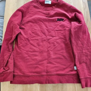 Mörkröd sweatshirt från Dobber - En enkel och stilren mörkröd sweatshirt från Dobber med rund halsringning och diskret broderad logga på bröstet. Tröjan har långa ärmar och är tillverkad i mjukt material, perfekt för kyligare dagar.