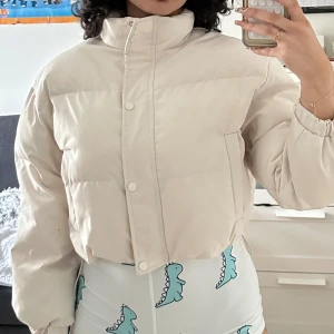 Beige pufferjacka med hög krage - Säljer en beige pufferjacka med hög krage. Jackan är croppad och man kan dra åt den vid midjan 