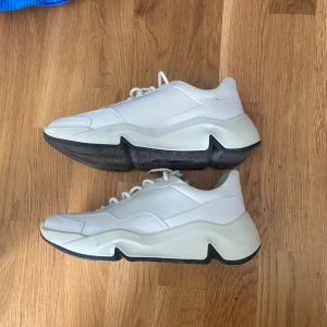 Chunky vita sneakers från ecco  - Säljer ett par chunky vita sneakers med tjock svart och vit sula. Skorna har snörning och en modern, sportig design med rund tå. Perfekta för dig som gillar streetwear och vill ha en stilren look.