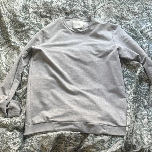 Ljusgrå sweatshirt från Jack & Jones - En basic ljusgrå sweatshirt från Jack & Jones Core-kollektionen. Tröjan har rund halsringning, ribbade muddar vid ärmslut och nederkant. Perfekt för en avslappnad stil och enkel att matcha med det mesta.