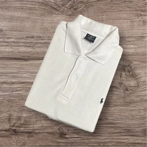 Ralph Lauren Piké – Vit (L)  - Ralph Lauren Piké – Vit (L) 🤍 Säljer en klassisk vit Ralph Lauren piké i storlek L. Tidlös och stilren design som passar perfekt både till vardag och finare tillfällen! Enkel att matcha med jeans eller chinos för en clean look. 	•	Färg: Vit 	•	Storlek: L (baserat på måtten) 	•	Mått: 📏 Längd 77 cm, armhåla till armhåla 61 cm, axel till axel 51 cm 	•	Nypris: ca 1800 kr 💸 	•	Skick: Billigt pris p.g.a. defekten som syns på sista bilden (syns ej när plagget används) ⚠️  111
