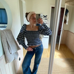 Svartvit rutig blus med puffärmar - Trendig svartvit rutig blus med smock och fyrkantig urringning. Puffiga långa ärmar och figurnära passform. Perfekt att styla med jeans för en cool look.