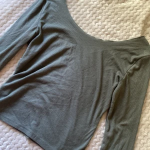 Ribbad grön långärmad topp - En stilren ribbad topp i grått med lång ärm och bred, rundad urringning. Toppens material är mjukt och stretchigt, perfekt för en enkel men snygg look. Passformen är normal och den är lätt att matcha med både jeans och kjol.