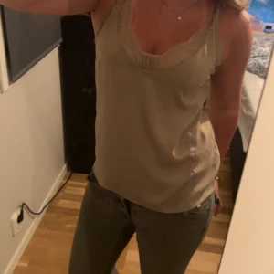 Beige linnetopp med spetsdetaljer - Säljer en beige linnetopp med tunna axelband och vacker spets längs urringningen. linnet är insytt där bak, går att enkelt ta bort.
