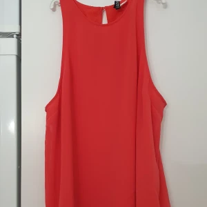 Linnetopp - Snygg röd/korall linnetopp från H&M med rund halsringning och knappdetalj i nacken. Toppen är ärmlös och har en luftig passform, perfekt för varma dagar. Tillverkad i ett lätt och skönt polyestertyg som faller fint.