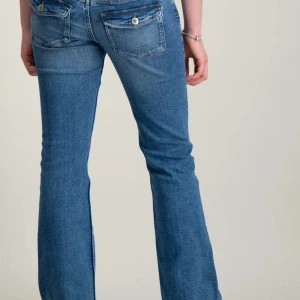 Lågmidjade jeans  - Säljer ett par klassiska blåa Lågmidjade jeans från Gina Tricot i storlek 164. Jeansen har bootcut-modell, dubbla knappar i midjan och snygga fickdetaljer bak med lock och knapp. Perfekta för hösten och vintern. 