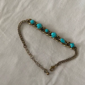 Armband - Ett snyggt och unikt armband från Montini i mörkguld (guld med en svartaktig ton), prytt med fina turkosa blå detaljer (inte äkta stenar). Använt ett par gånger men ser fortfarande helt nytt ut. Perfekt för att ge din outfit en elegant och annorlunda touch.