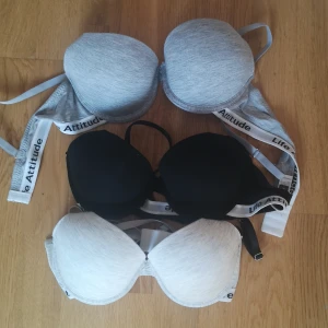 3-pack Shein bh-toppar med textband - Säljer ett 3-pack bh-toppar från Shein i färgerna grå, svart och ljusgrå. Alla har breda axelband med texten 'Life Attitude' och vadderade kupor. Materialet är mjukt och stretchigt med 95% rayon och 5% spandex för skön passform.