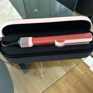 Dyson hårstyler i rosa och rött - Säljer en snygg Dyson hårstyler i metallic rött och ljusrosa med svart sladd. Kommer i ett stilrent fodral som skyddar verktyget. Perfekt för att fixa håret snabbt och enkelt med en lyxig känsla.