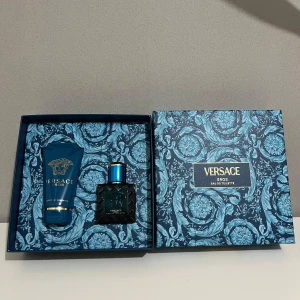 Versace Eros presentbox parfymset - Lyxigt presentset från Versace Eros med Eau de Toilette och duschgel. Flaskan är fyrkantig i mörkblått glas med gulddetaljer och Medusa-logga. Duschgelen kommer i en matchande blå tub med guldtext. Allt levereras i en elegant blå mönstrad box.