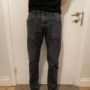 Tiger of Sweden Jeans - Säljer ett par snygga gråa Tiger of Sweden Jeans i färgen kid jet black. De är i storlek W30 L32. Jeansen är i bra skick bortsett från defekten i bild 4 och slitningen vid hälen i bild 5. Jag säljer nu dessa för endast 99kr. Hör av er vid frågor eller funderingar.