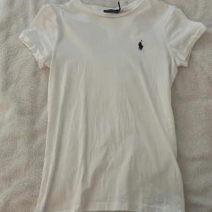 Vit t-shirt från Polo Ralph Lauren - Vit klassisk t-shirt från Polo Ralph Lauren med korta ärmar och rund hals. Liten broderad logga i mörkblått på bröstet. Knappt använd 