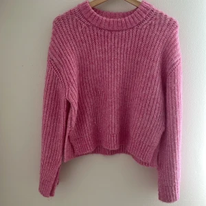 Rosa stickad tröja från Gina Tricot - Supermysig rosa stickad tröja från Gina Tricot med grov ribbstickning och rund hals. Tröjan har lång ärm och en lite loose passform, perfekt för lager på lager. Färgen är en härlig ljusrosa som verkligen poppar.