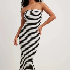 Randig axelbandslös långklänning - Säljer en tight, axelbandslös långklänning med svartvita horisontella ränder. Klänningen är ribbad och har en slits baktill för extra rörelsefrihet. Perfekt för dig som gillar en stilren och trendig look. Är från NAKD i storlek S!