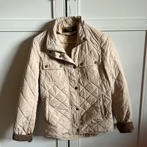 Beige quiltad jacka Massimo Dutti - Quiltad beige jacka från Massimo Dutti med bruna mockadetaljer på armbågar och krage. Jackan har tryckknappar, dragkedja, två bröstfickor och två sidfickor. Perfekt för höst och vår, snygg och stilren med klassiska detaljer. Priset är inte hugget i sten. Jackan köptes begagnat, därför det lite lägre priset. Ni är varmt välkomna att lägga prisförslag, ställa frågor osv.😁