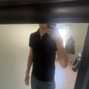 Svart t-shirt med dragkedja - Svart t-shirt med korta ärmar och en snygg liten dragkedja vid halsen. Enkel och stilren design som passar till det mesta. Skön passform och perfekt för dig som gillar en clean look.