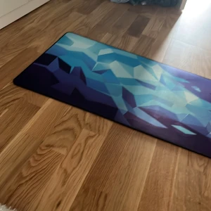  En musmatta som är knappt använd och är i bra skick. Den är jättestor - Bilderna visar en stor musmatta från Xtrfy med ett coolt, geometriskt mönster i blått och lila. Perfekt för gaming eller studier, ger din setup en modern och färgstark touch. Mattan ser ut att vara i fint skick och passar dig som vill ha stil och funktion på skrivbordet.
