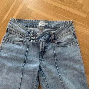 Ljusblå bootcut jeans från 157 - Snygga ljusblå jeans från 157 med bootcut passform och markerade sömmar framtill. Jeansen har dubbla knappar i midjan och klassiska fem fickor. Perfekta för dig som gillar retrovibbar och vill ha ett par jeans som sticker ut.