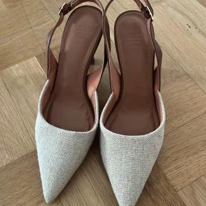 Beige pumps med spetsig tå och klack - Stilrena pumps från COS i beige textil med spetsig tå och smal klack. Skorna har bruna detaljer i skinn och justerbar rem runt hälen. Perfekta för dig som gillar minimalistisk och modern design.