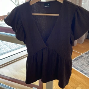 Brun blus med volangärm Gina Tricot - Supersöt brun blus från Gina Tricot i storlek XS. Toppen har djup v-ringning, voluminösa volangärmar och en lätt rynkad midja som ger en flowy siluett. Materialet är strukturerat och känns mjukt mot huden. Perfekt för dig som gillar trendiga detaljer!