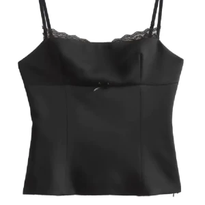 Svart satinlinnetopp med spets - Supersnygg svart linnetopp i satin med tunna axelband och spetsdetalj längs urringningen från Zara. Toppen har en liten rosett framtill och sitter figurnära med croppad passform. Perfekt att styla med jeans eller kjol för en trendig look. Är i storlek M men skulle säga att den sitter bättre på en S💗