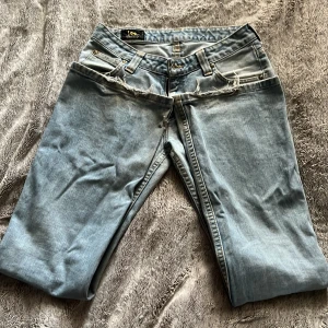 Ljusblå Lee jeans bootcut - Säljer ett par ljusblå jeans från Lee med klassisk femficksdesign och bootcut-snitt. Jeansen har slitna detaljer vid fickorna. De är lite mittemellan från low waist till mid waist. Storlek 34 vilket motsvarar xs/s 