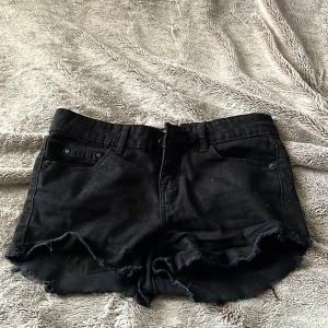 Svarta jeansshorts med fransig kant - Svarta jeansshorts från gina , fransig kant nertill och klassisk femficksdesign. Shortsen har bälteshällor och knappstängning framtill. Storlek 24 vilket motsvarar xxs 
