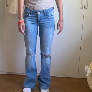 Lågmidjade Ljusblå bootcut jeans med hål - Säljer ett par lågmidjade ljusblå jeans med bootcut-modell.  Supersnygga och sköna jeans💕💕Har slitage längst ner pga hamnat under skon. Jag är 1,65 på bilden😊