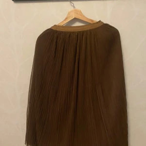 Hell ny Brun plisserad långkjol - Hell ny Snygg brun långkjol med plisserat tyg och flowig känsla. Perfekt för dig som gillar en stilren och trendig look. Kjolen har resår i midjan för skön passform och är lätt att matcha med både sneakers och boots. Storlek M