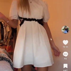 Vit kortklänning med svarta detaljer - Supersöt vit kortklänning med puffärmar och svarta volangdetaljer runt midjan. Klänningen har en luftig passform och är perfekt för dig som gillar en romantisk och trendig stil. Passar lika bra till sneakers som till klackar.