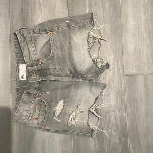 Grå jeansshorts från Zara - Trendiga grå jeansshorts från Zara med fransiga kanter och slitningar framtil. Materialet är robust denim som ger en cool vintagekänsla. Storlek 32, säljer pågrund av att dom är försmå.