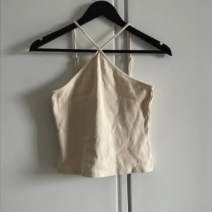 Beige ribbad linnetopp med smala band - Säljer en beige croppad linnetopp med smala axelband. Toppen är ribbad och har en enkel, stilren design med lätt A-linjeform. Perfekt för varma dagar och enkel att matcha med jeans eller kjol.