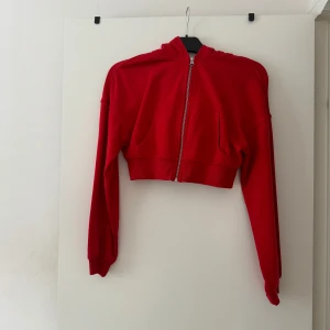 Röd croppad hoodie från Divided - Snygg röd croppad hoodie från Divided med dragkedja framtill och huva. Tröjan har långa ärmar och ribbade muddar. Perfekt för dig som gillar en sportig och trendig stil. Tillverkad i mjuk bomullsmix för extra komfort. Passade bra för mig med storlek S. 