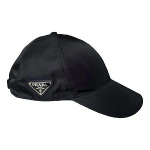 Svart keps från P - Snygg svart keps från Prada med klassisk böjd skärm och ikonisk metallogo på sidan. Tillverkad i glansig nylon som ger en lyxig känsla. Perfekt accessoar för att lyfta din outfit med en exklusiv touch.