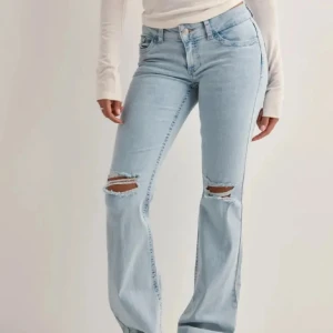 Ljusblå bootcut jeans med slitningar - Snygga ljusblå jeans med bootcut passform och slitna hål över knäna. Jeansen har klassisk femficksdesign, normal midja och är tillverkade i mjukt denimtyg. Perfekta för en avslappnad och trendig look.