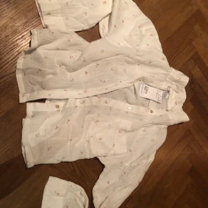 Vit blommig skjorta från H&M - Superfin vit skjorta från H&M med små blommiga detaljer i rosa och grönt. Skjortan har en avslappnad passform, knappar framtill och är tillverkad i ett lätt och luftigt bomullstyg. Perfekt för vår och sommar när du vill ha en chill och söt look. HELT NY!❤️❤️❤️ ALDRIG ANVÄND!